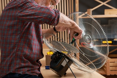 Photo of Relaxing hobby. Senior man repairing fan with screwdriver in workshop, closeup