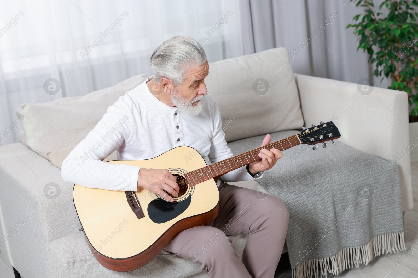 Photo of Relaxing hobby. Senior man playing guitar on sofa at home