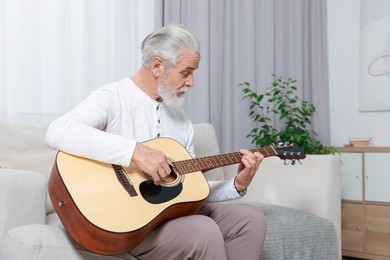 Photo of Relaxing hobby. Senior man playing guitar on sofa at home