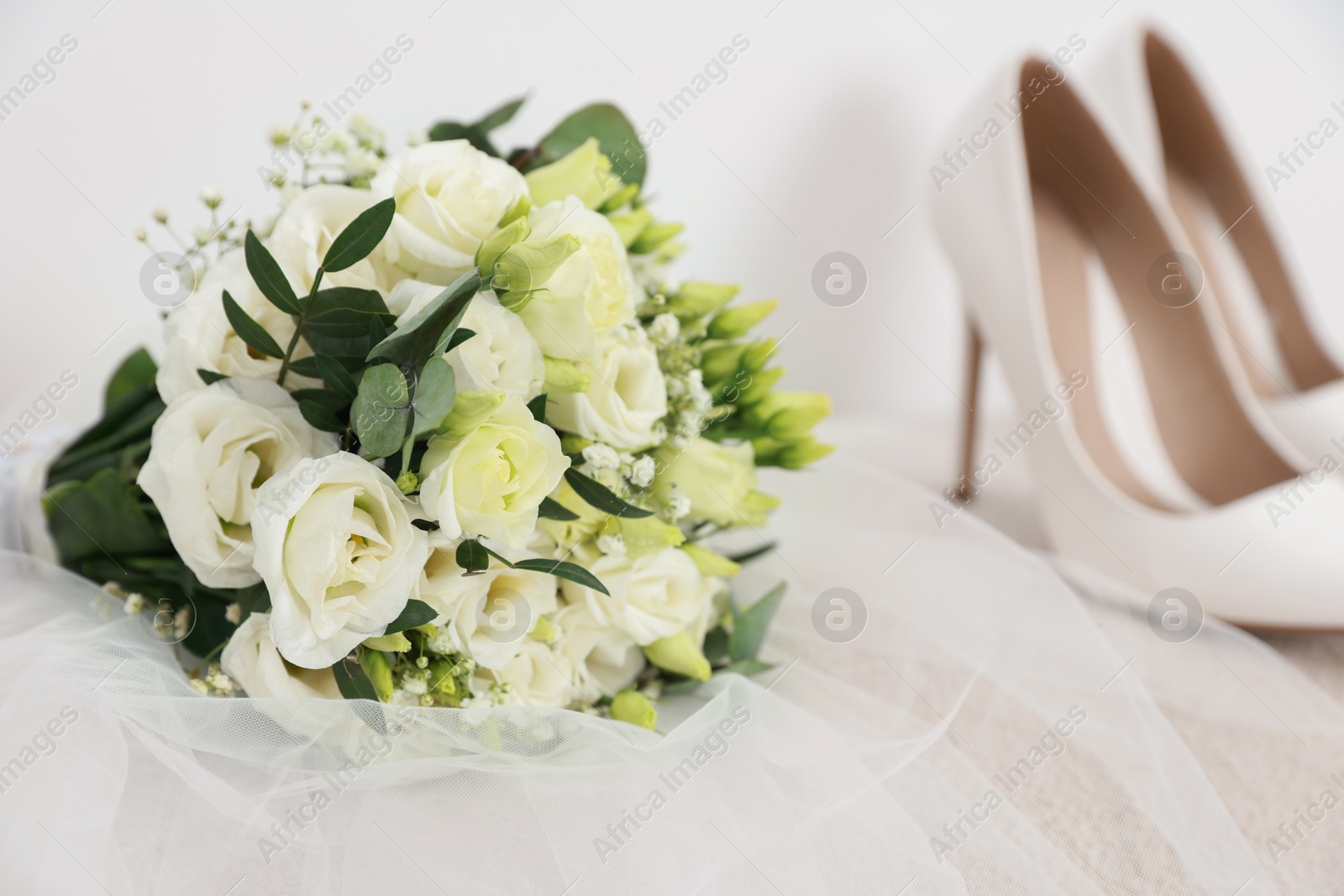 Photo of Beautiful wedding bouquet, veil and bridal shoes on light background, closeup