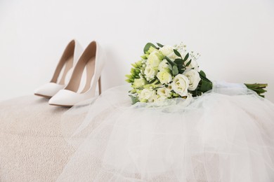 Photo of Beautiful wedding bouquet, veil and bridal shoes on pouf against light background