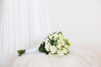 Photo of Beautiful wedding bouquet and veil on pouf against light background, space for text