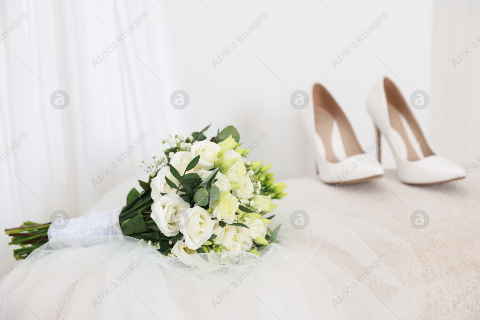 Photo of Beautiful wedding bouquet, veil and bridal shoes on pouf against light background