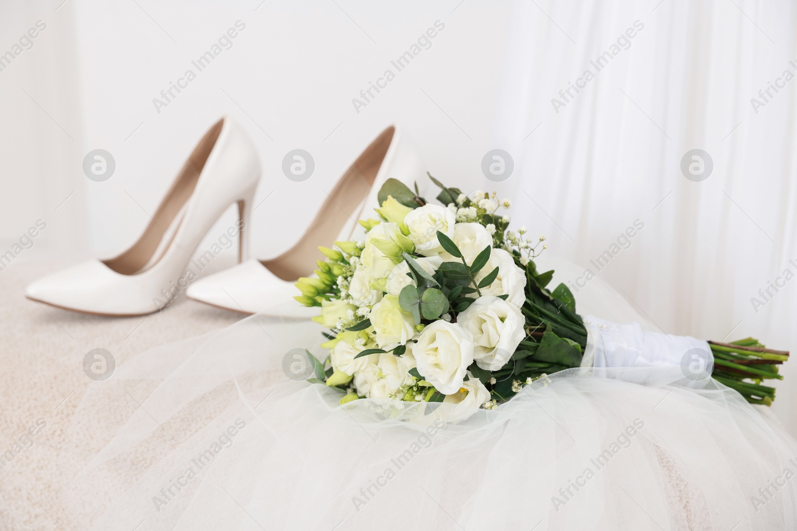 Photo of Beautiful wedding bouquet, veil and bridal shoes on pouf against light background