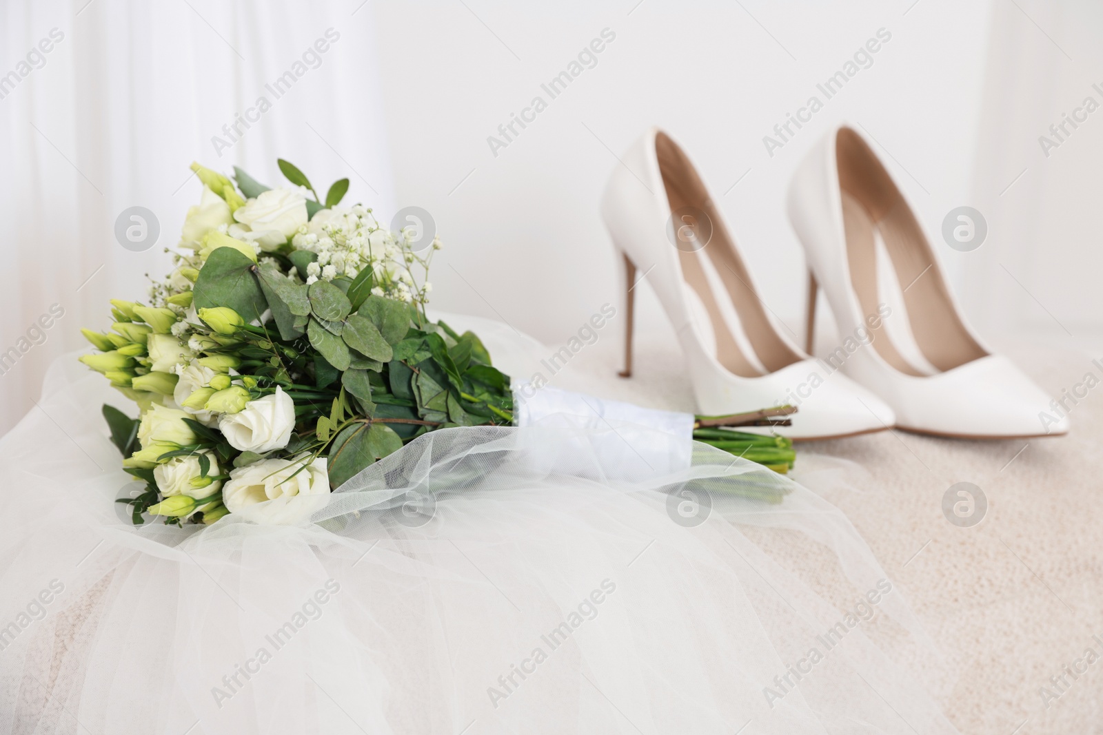 Photo of Beautiful wedding bouquet, veil and bridal shoes on pouf against light background