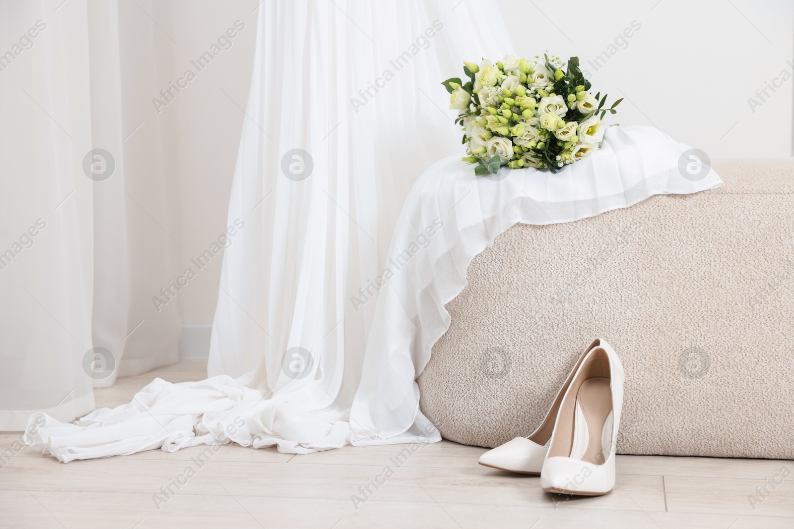 Photo of Beautiful wedding bouquet on pouf, dress and bridal shoes indoors