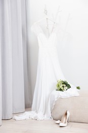 Photo of Beautiful wedding bouquet on pouf, dress and bridal shoes indoors