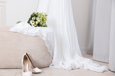 Photo of Beautiful wedding bouquet on pouf, dress and bridal shoes indoors