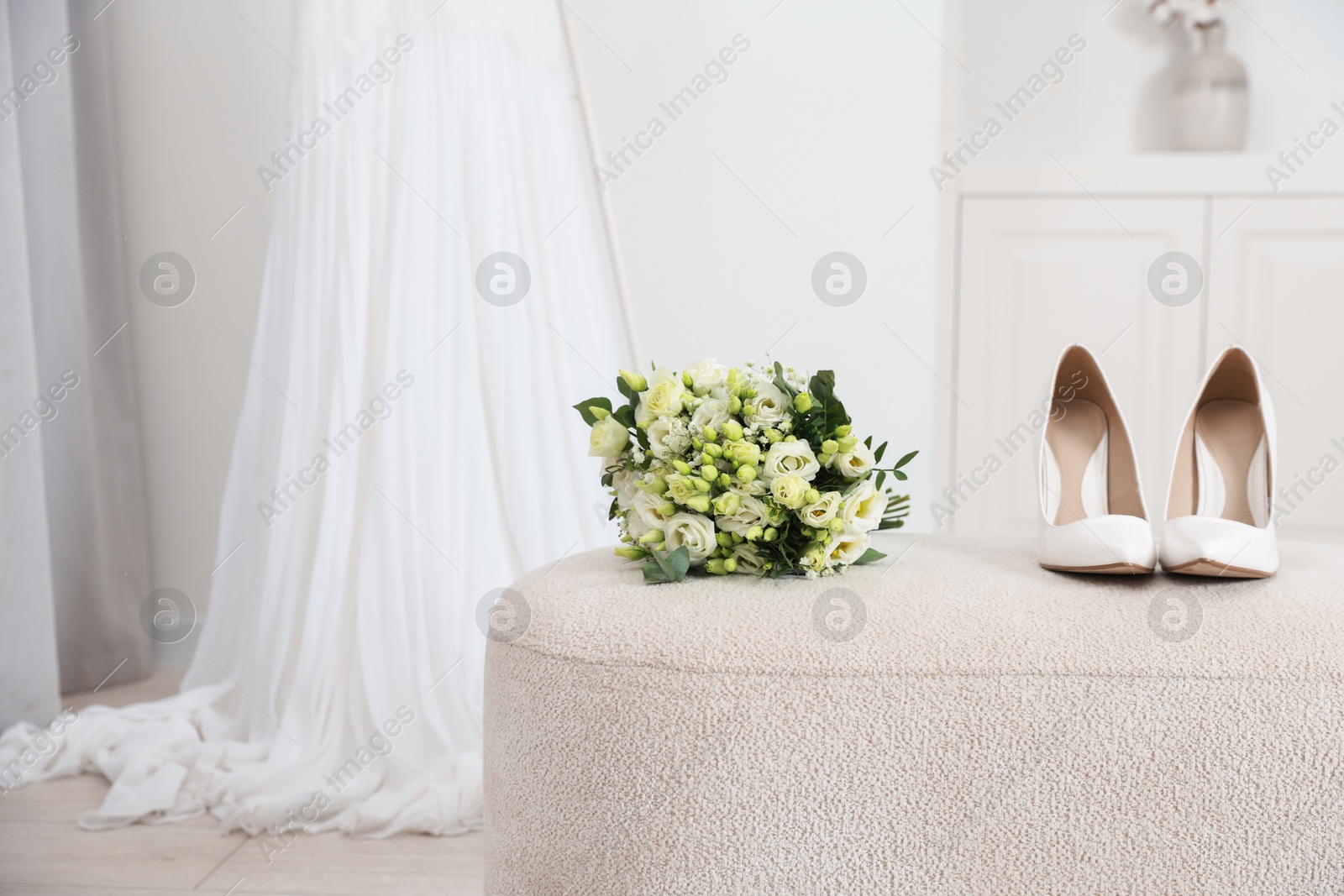 Photo of Beautiful wedding bouquet and bridal shoes on pouf indoors