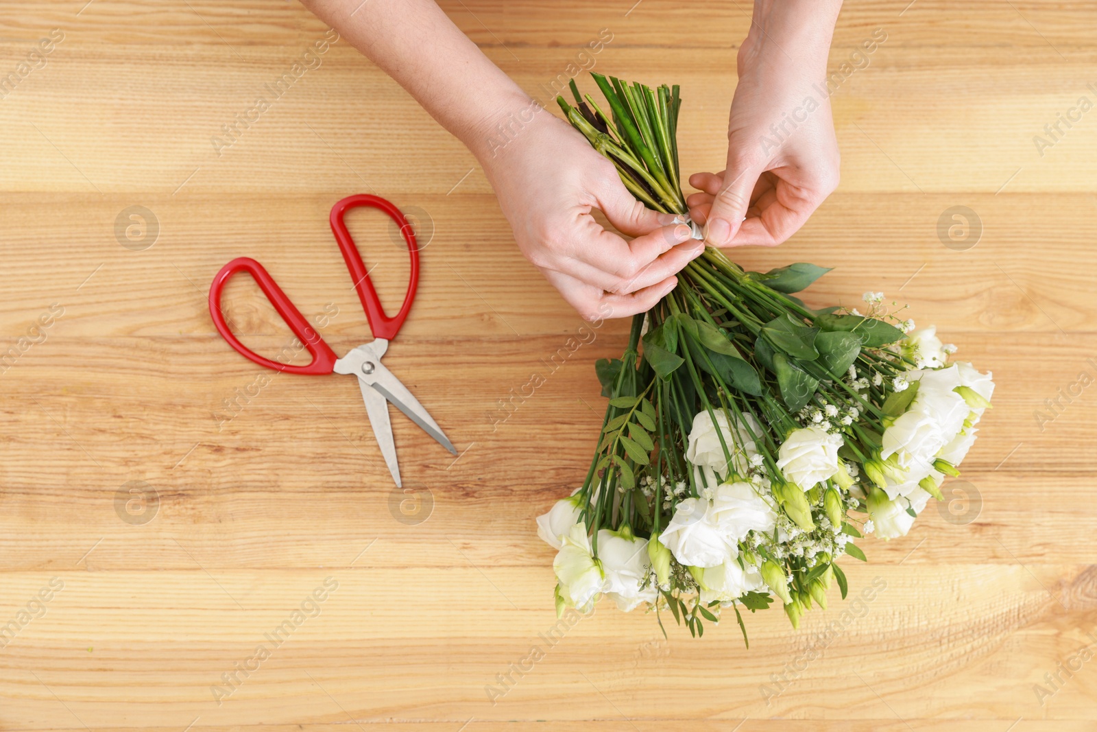 Photo of Florist making beautiful wedding bouquet at wooden table, top view