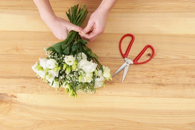 Photo of Florist making beautiful wedding bouquet at wooden table, top view