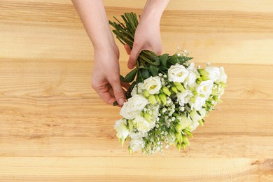 Photo of Florist with beautiful wedding bouquet at wooden table, top view