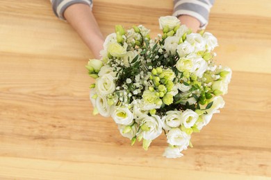 Photo of Florist with beautiful wedding bouquet at wooden table, top view