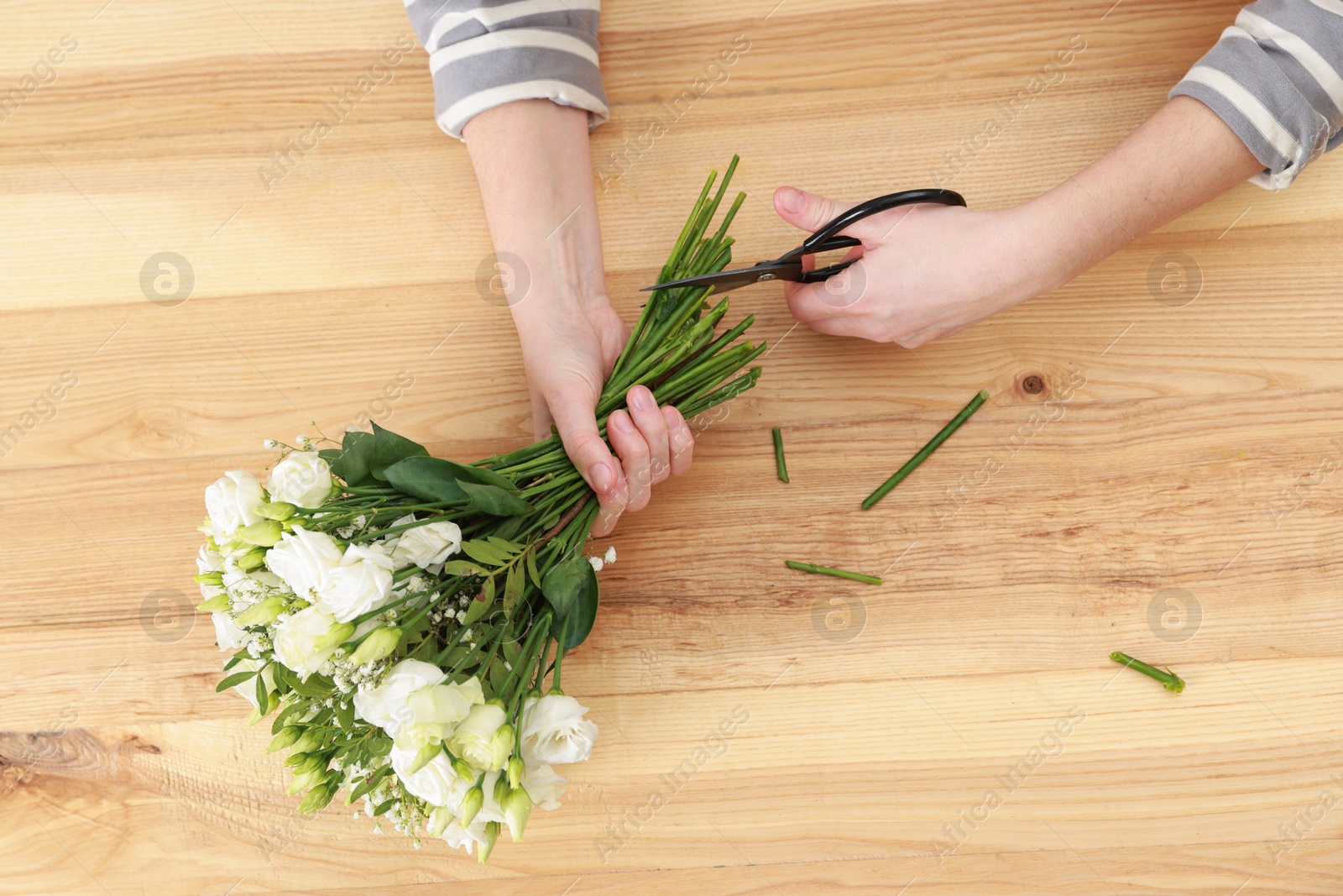 Photo of Florist making beautiful wedding bouquet at wooden table, top view