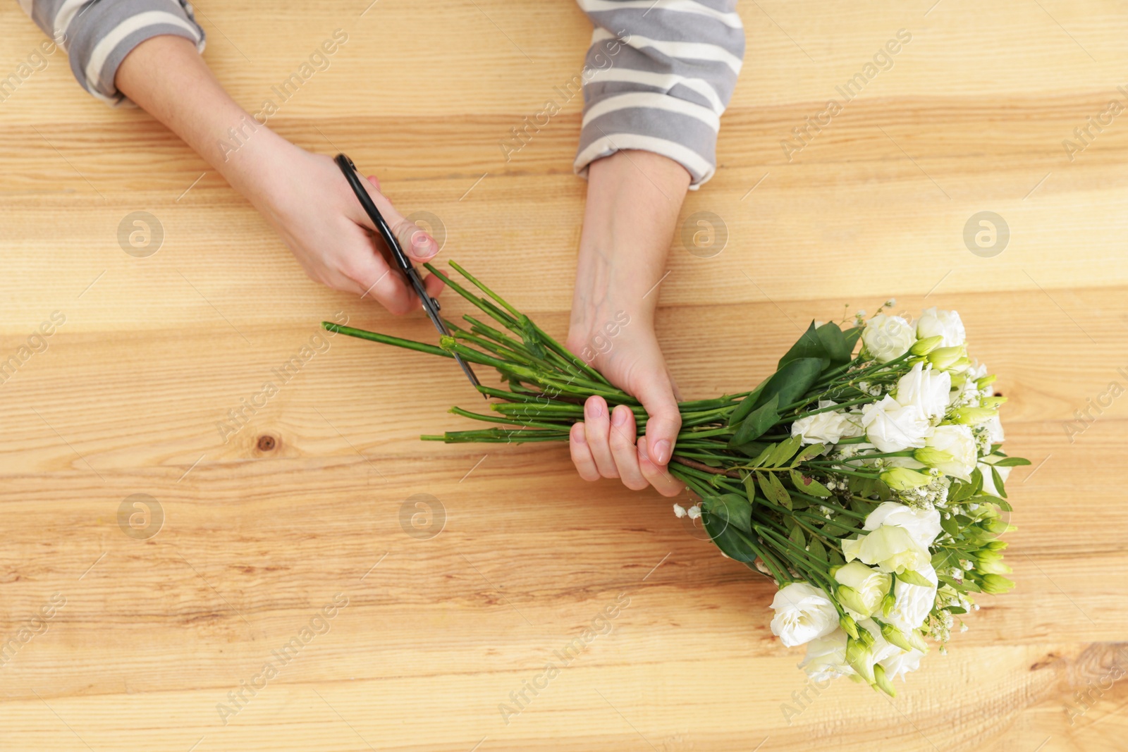 Photo of Florist making beautiful wedding bouquet at wooden table, top view