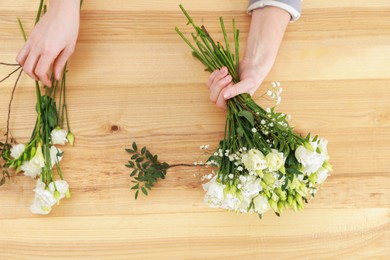 Photo of Florist making beautiful wedding bouquet at wooden table, top view