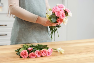 Photo of Florist making beautiful wedding bouquet at wooden table indoors, closeup