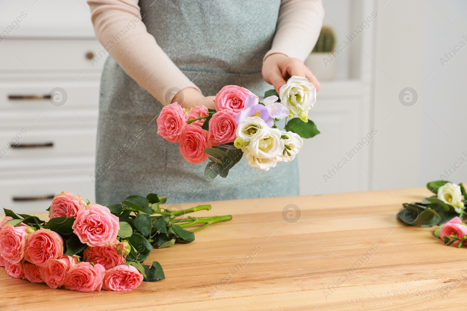 Photo of Florist making beautiful wedding bouquet at wooden table indoors, closeup