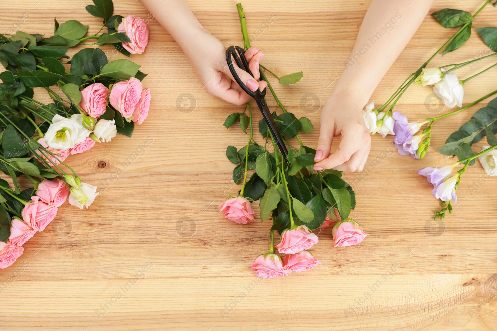 Photo of Florist making beautiful wedding bouquet of fresh rose flowers at wooden table, top view