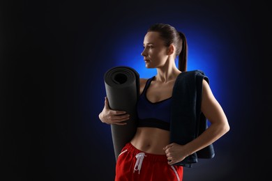 Photo of Sporty woman with terry towel and fitness mat on dark blue background, space for text