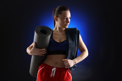 Photo of Sporty woman with towel and fitness mat on dark blue background