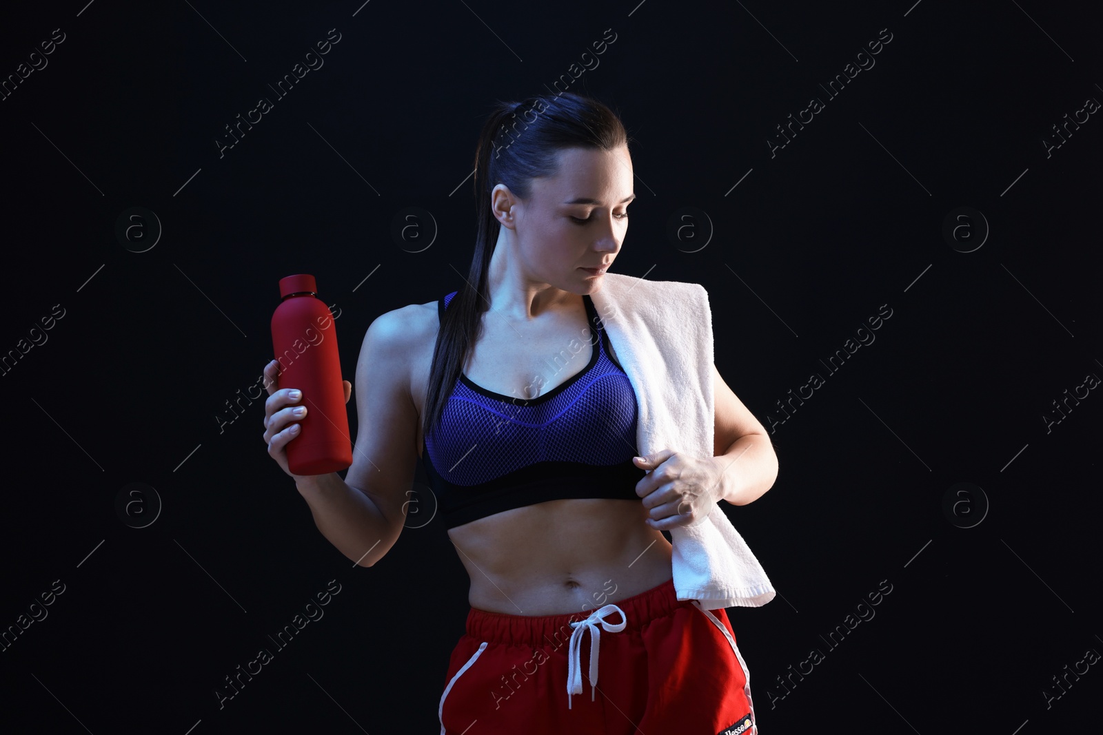 Photo of Sporty woman with terry towel and water bottle on dark background