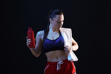 Photo of Sporty woman with terry towel and water bottle on dark background