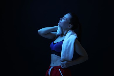 Photo of Sporty woman with terry towel on dark background in neon light