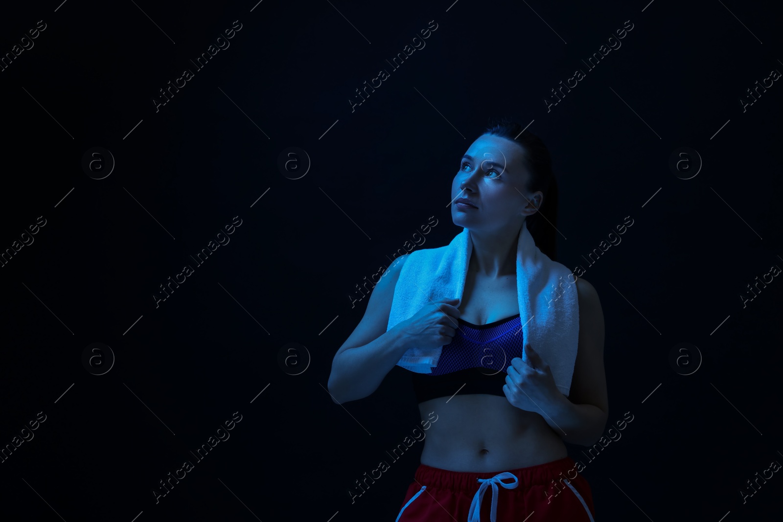 Photo of Sporty woman with terry towel on dark background in neon light. Space for text