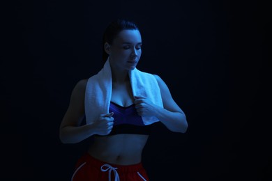 Photo of Sporty woman with terry towel on dark background in neon light. Space for text