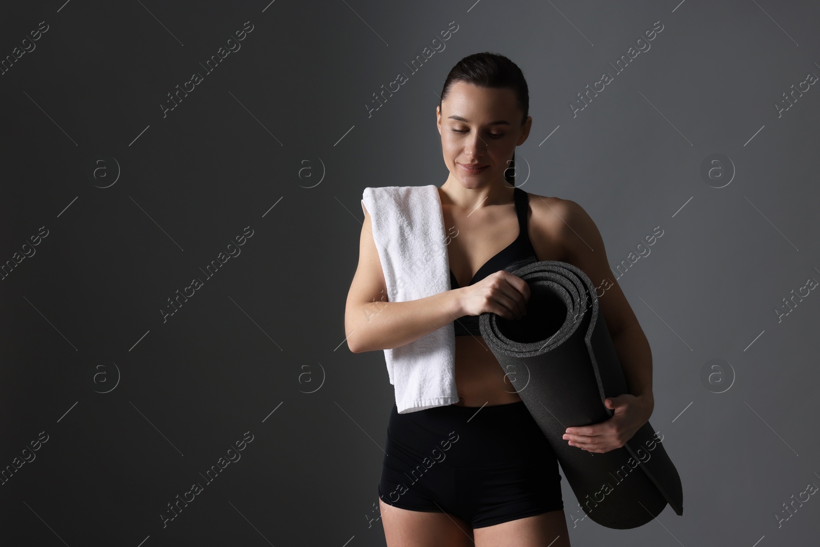 Photo of Sporty woman with terry towel and fitness mat on dark grey background, space for text