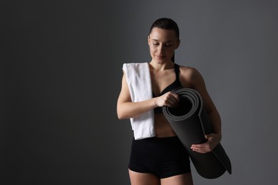 Photo of Sporty woman with terry towel and fitness mat on dark grey background, space for text