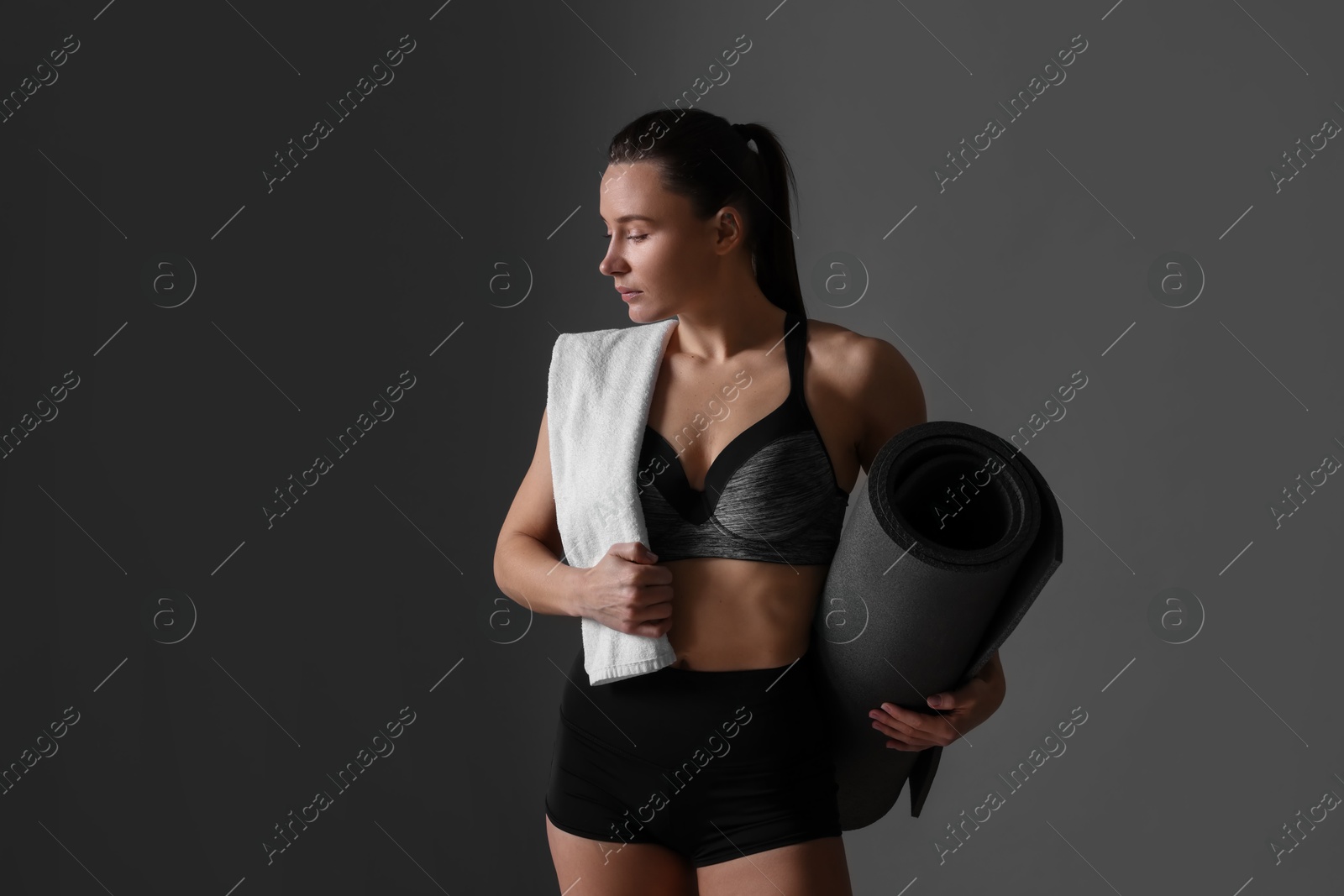 Photo of Sporty woman with terry towel and fitness mat on dark grey background