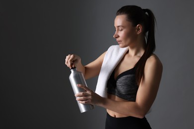 Photo of Sporty woman with towel and water bottle on dark grey background, space for text