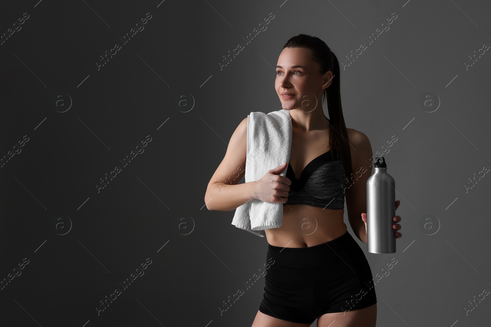 Photo of Sporty woman with towel and water bottle on dark grey background, space for text