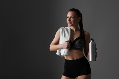 Photo of Sporty woman with towel and water bottle on dark grey background, space for text