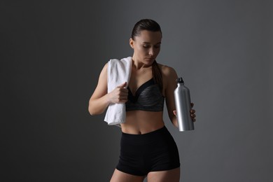 Photo of Sporty woman with towel and water bottle on dark grey background