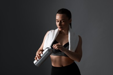 Photo of Sporty woman with towel and water bottle on dark grey background