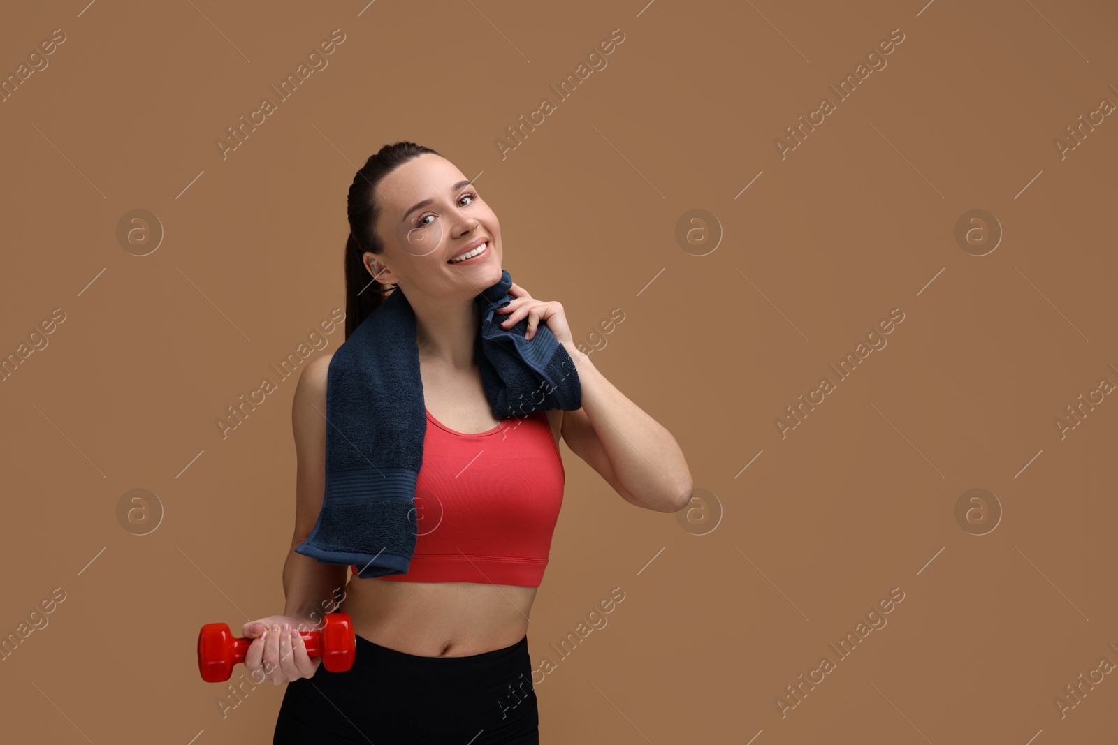 Photo of Sporty woman with towel and dumbbell on brown background, space for text