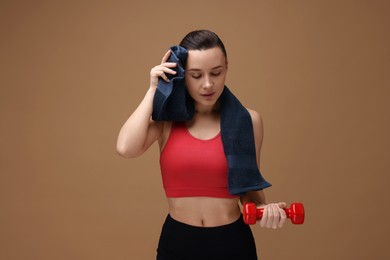 Photo of Sporty woman with towel and dumbbell on brown background