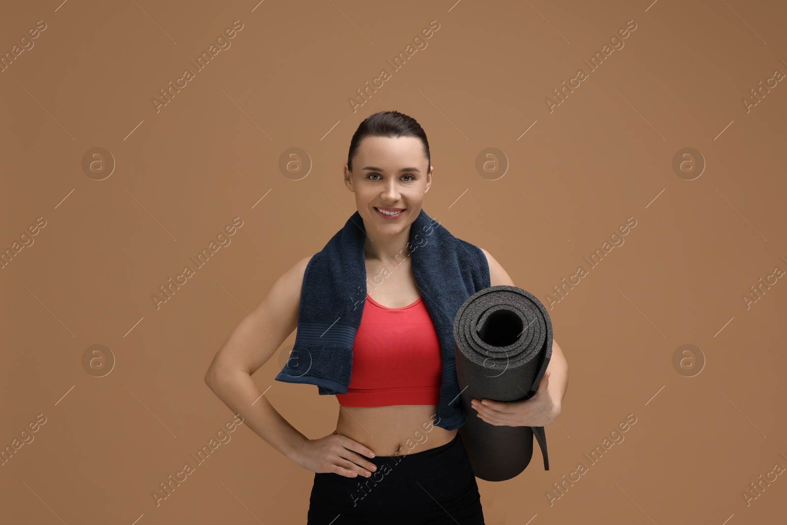 Photo of Sporty woman with terry towel and fitness mat on brown background