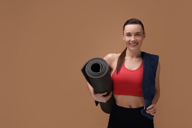 Photo of Sporty woman with terry towel and fitness mat on brown background. Space for text