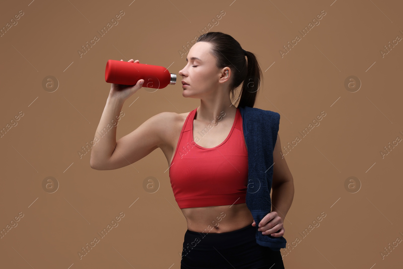 Photo of Sporty woman with towel drinking water on brown background