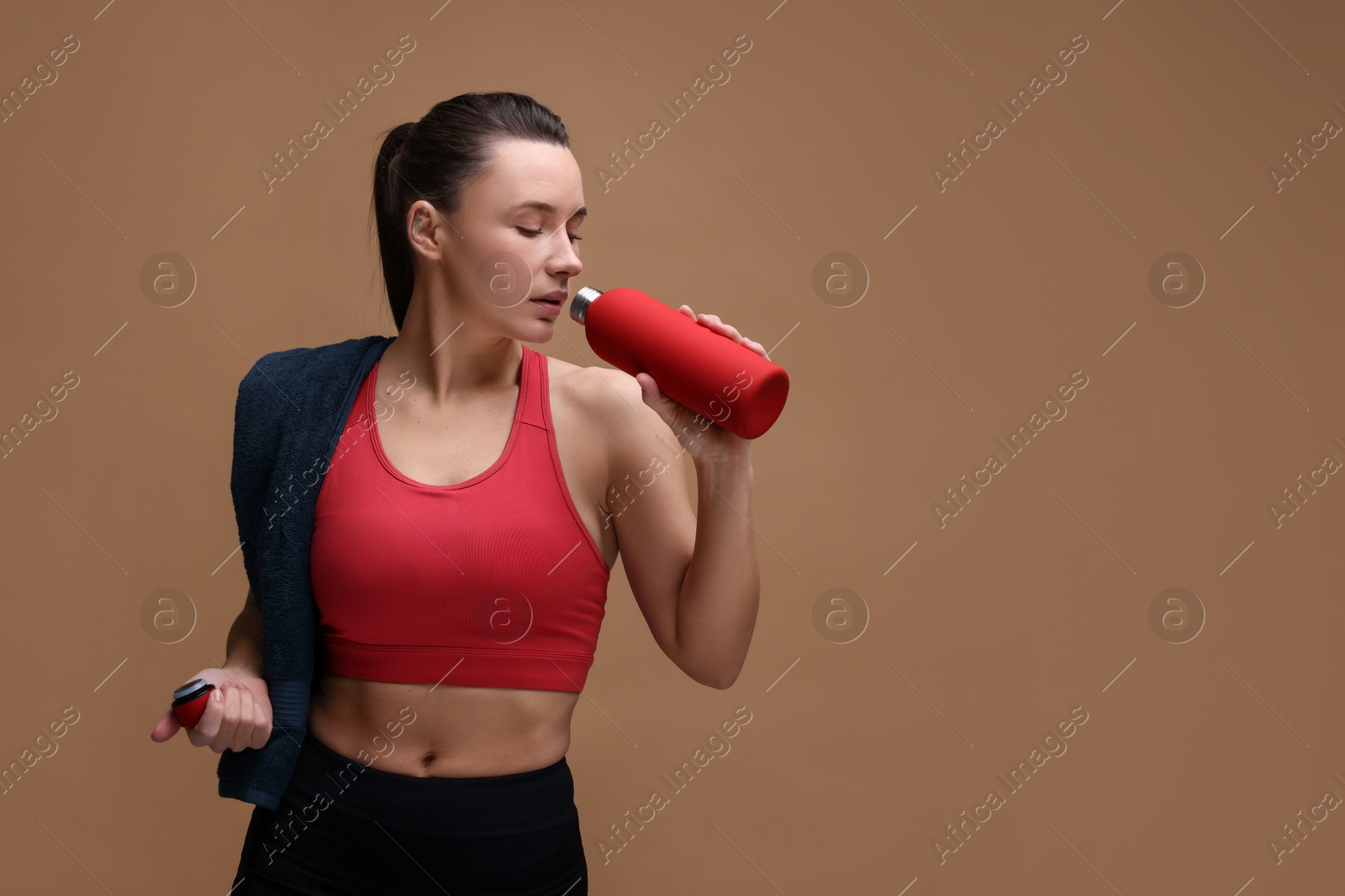 Photo of Sporty woman with towel drinking water on brown background