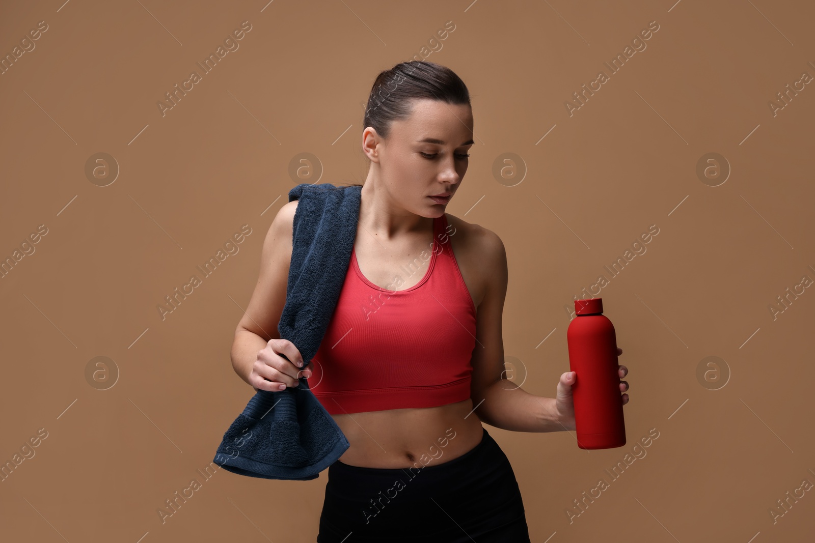 Photo of Sporty woman with towel and water bottle on brown background