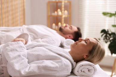 Photo of Couple in bathrobes lying on massage tables in spa salon, selective focus