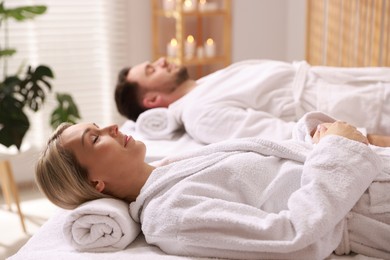 Photo of Couple in bathrobes lying on massage tables in spa salon, selective focus