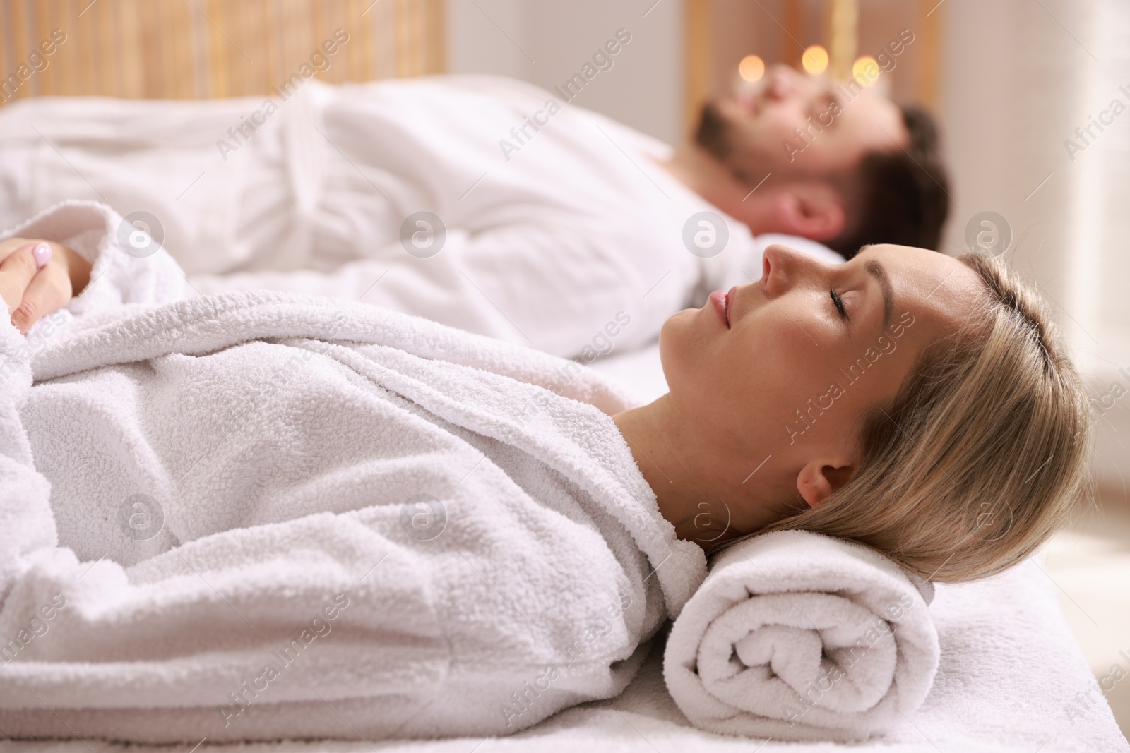 Photo of Couple in bathrobes lying on massage tables in spa salon, selective focus