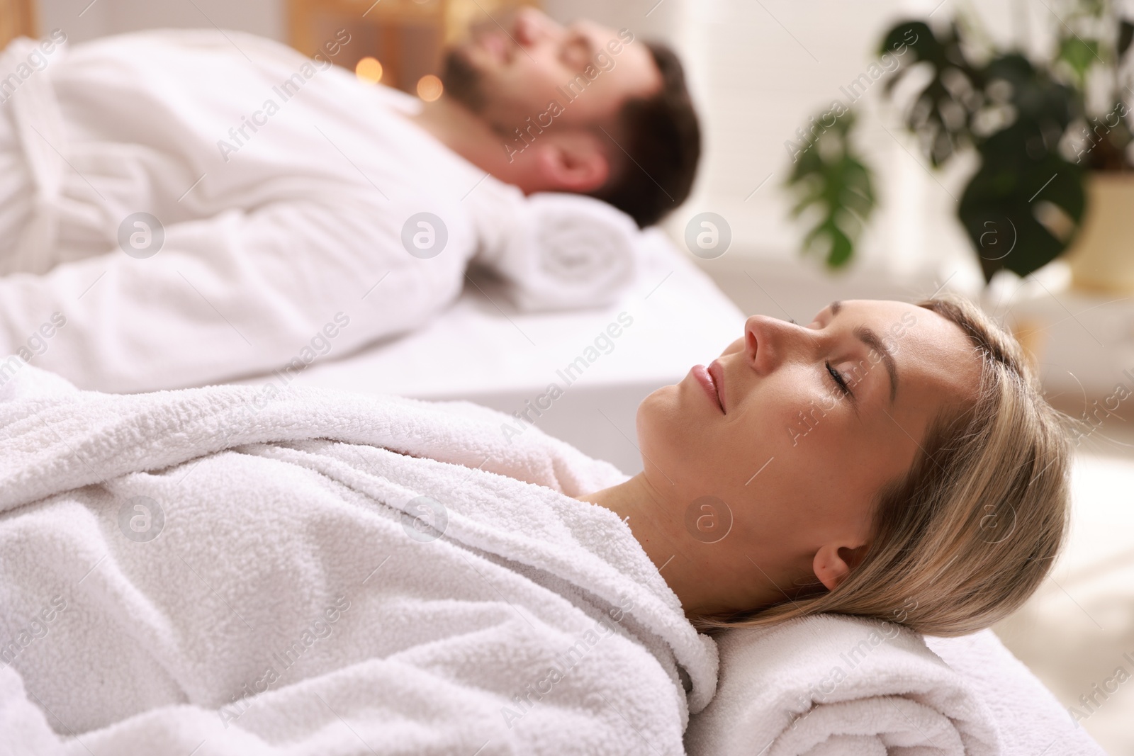 Photo of Couple in bathrobes lying on massage tables in spa salon, selective focus