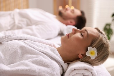 Photo of Couple in bathrobes lying on massage tables in spa salon, selective focus